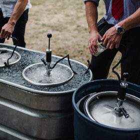 Men pouring beer from keg in cooling bath at barbecue, cropped